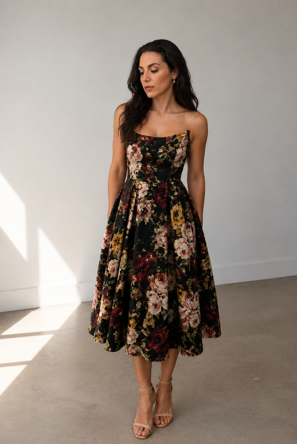A woman stands indoors wearing the Sarvin Golshifteh Floral Corset Midi Dress with her hands in the pockets, long dark hair down, and looking slightly downward.