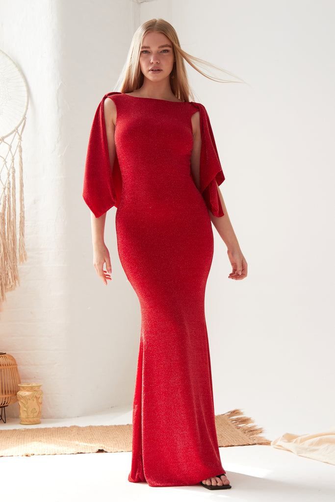 A woman in a Sarvin Red Cowl Back Gown is standing in front of a white wall.