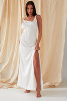 The model is wearing a Sarvin Asymmetric White Maxi Dress with a slit.