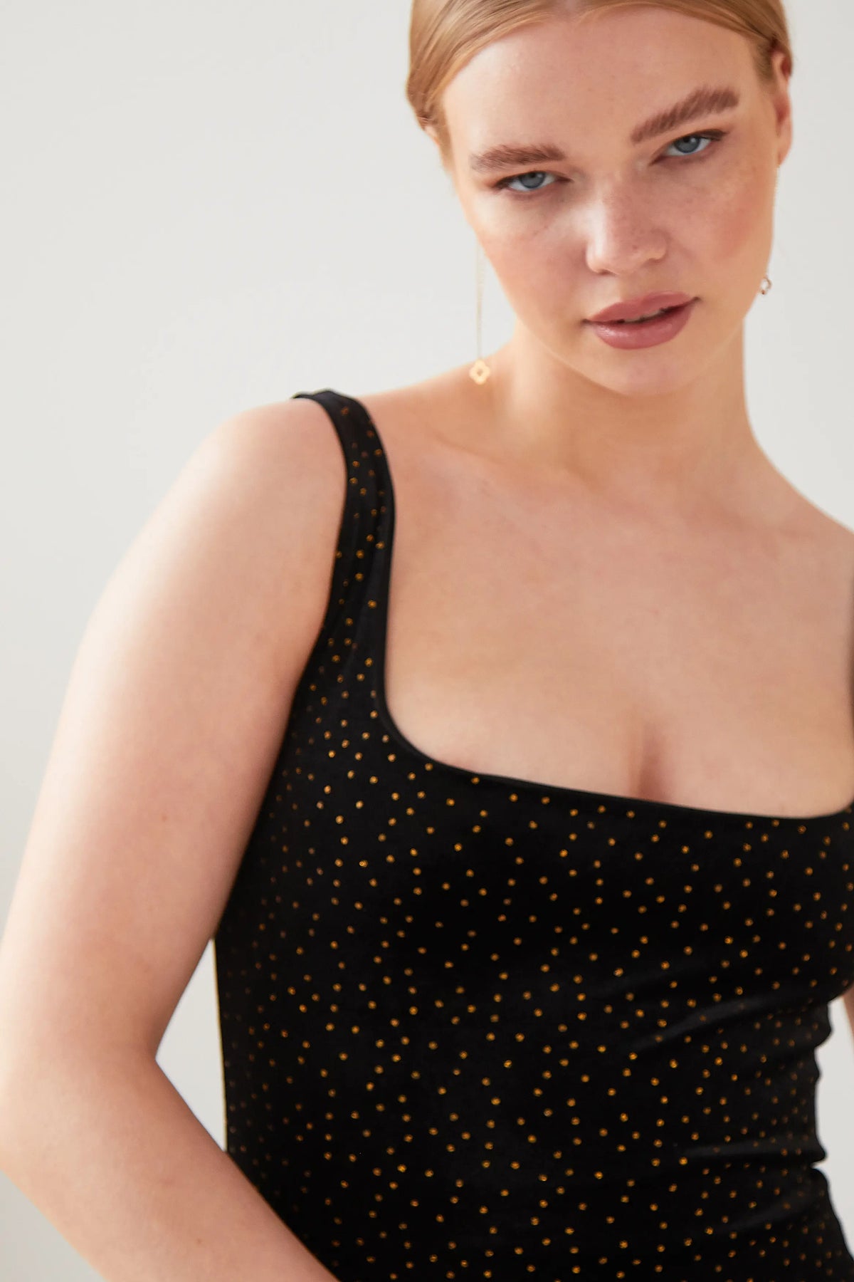 A person with light skin and blonde hair wears the Sarvin Black Polka Dot Dress, looking into the camera with a neutral expression against a plain, light-colored background.