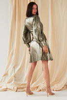 A woman poses before beige draped fabric, wearing the Sarvin Long Sleeve Sequin Wrap Dress and nude heels—an eye-catching choice for evening wear.