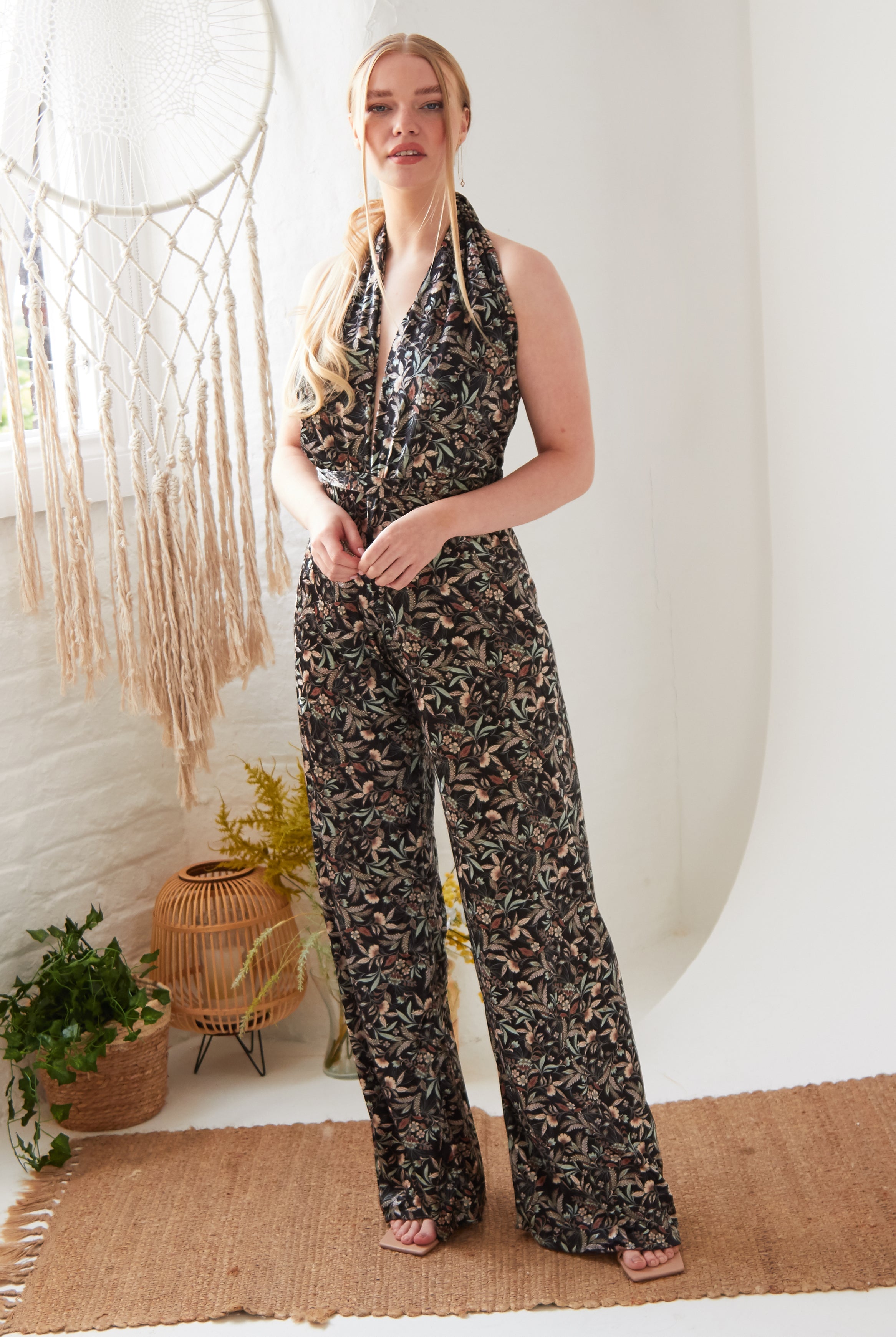 A woman in a Floral Velvet Backless Jumpsuit by Sarvin, standing in a white room.