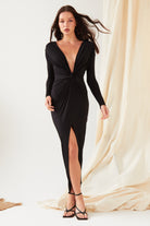 A woman stands against a neutral backdrop wearing Sarvin's long-sleeve black dress with a deep V-neckline and twist waist detail, paired with Circle Shape 18K Gold Drop Earrings and strappy heels for an effortlessly sophisticated look.