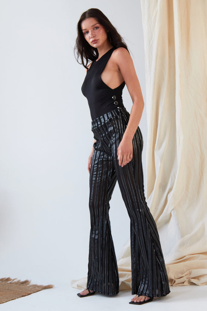 The model is wearing Sarvin's Flare Trousers In Metallic Stripe and a black top.