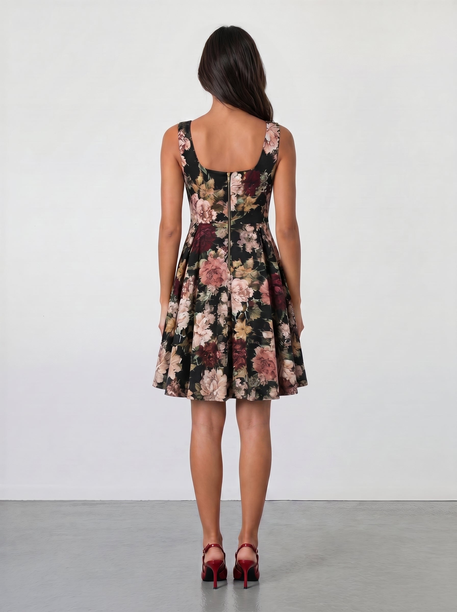 A woman with long brown hair faces away, wearing the Sarvin Golha Floral Corset Dress—sleeveless, knee-length, with a pink and beige floral pattern—and red high heels, set against a plain light background.