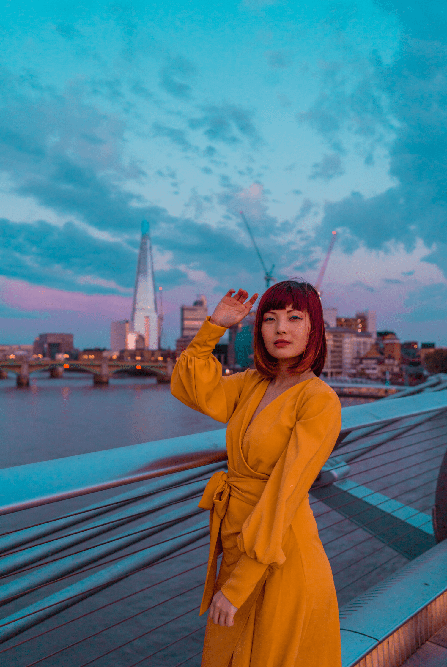 Wearing the Sarvin Mustard Wrap Maxi Dress with balloon bishop sleeves, a person stands on a bridge at sunset, city skyline and the Shard visible in the background under a cloudy sky.