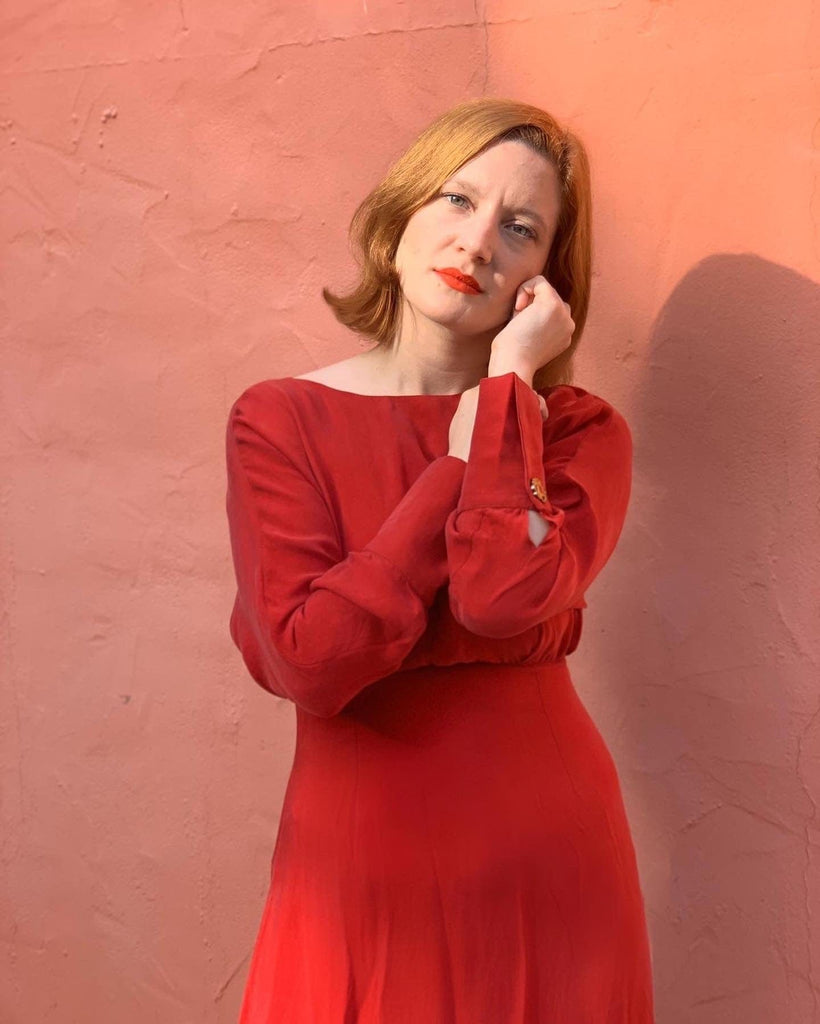 a woman in a Sarvin Long Sleeve Midi Dress leaning against a wall.