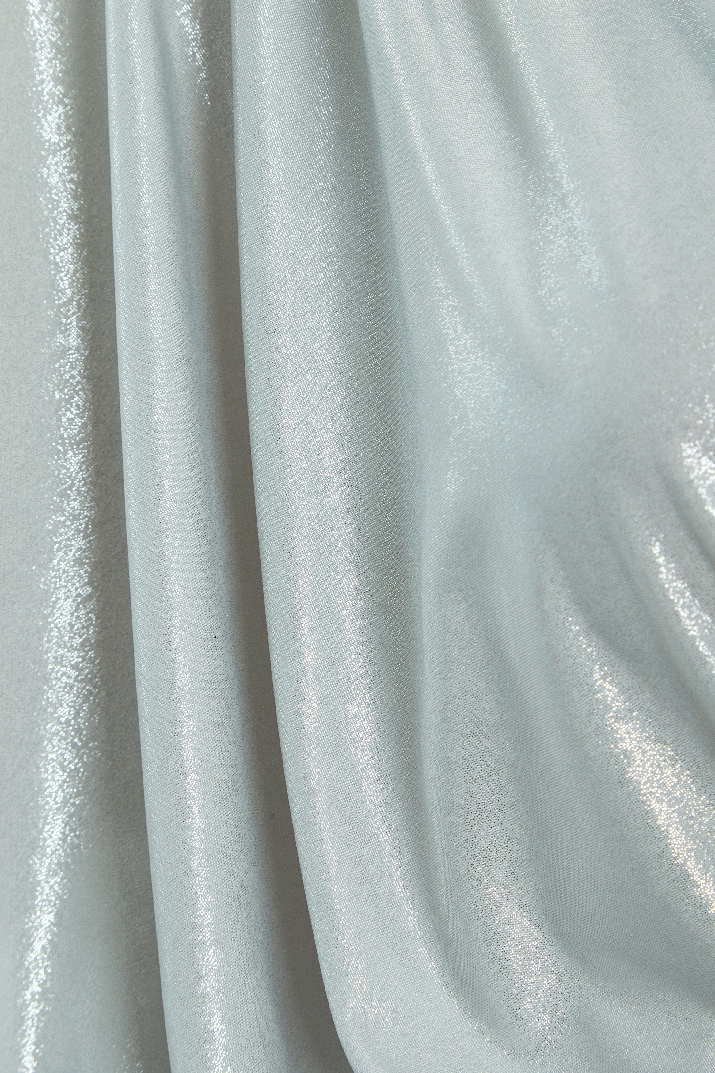 A close-up of silver metallic fabric with a shiny, reflective surface and soft folds—ideal for creating the Sarvin Batwing Sleeve Midi Dress, perfect for a show-stopping party look.
