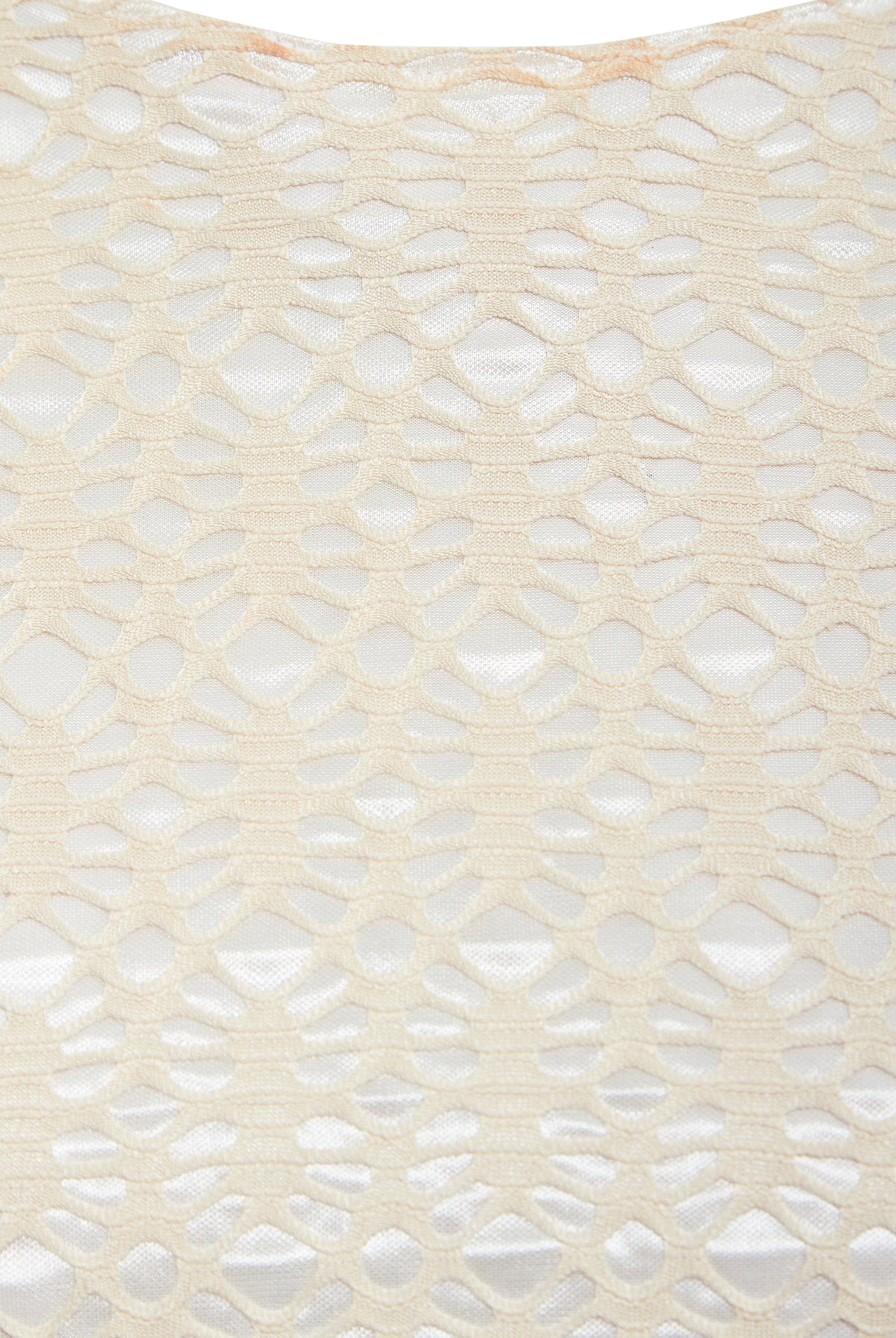 Close-up of Sarvin's Ivory Lace Backless Dress: cream-colored lace with a geometric hexagonal and oval pattern overlays a white background, showcasing the dress's textured detail.