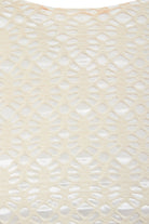 Close-up of Sarvin's Ivory Lace Backless Dress: cream-colored lace with a geometric hexagonal and oval pattern overlays a white background, showcasing the dress's textured detail.