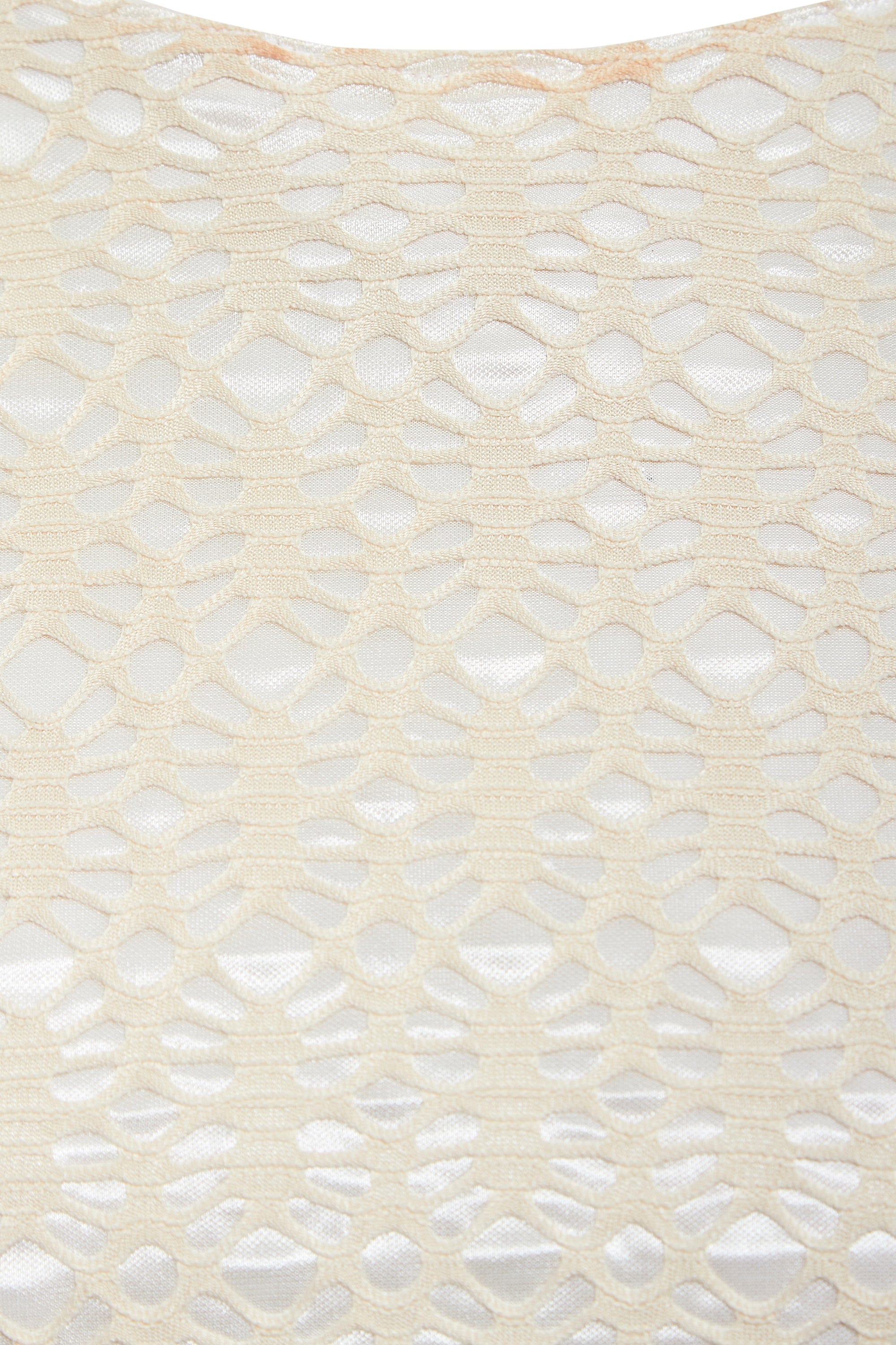 Close-up of Sarvin's Ivory Lace Backless Dress: cream-colored lace with a geometric hexagonal and oval pattern overlays a white background, showcasing the dress's textured detail.