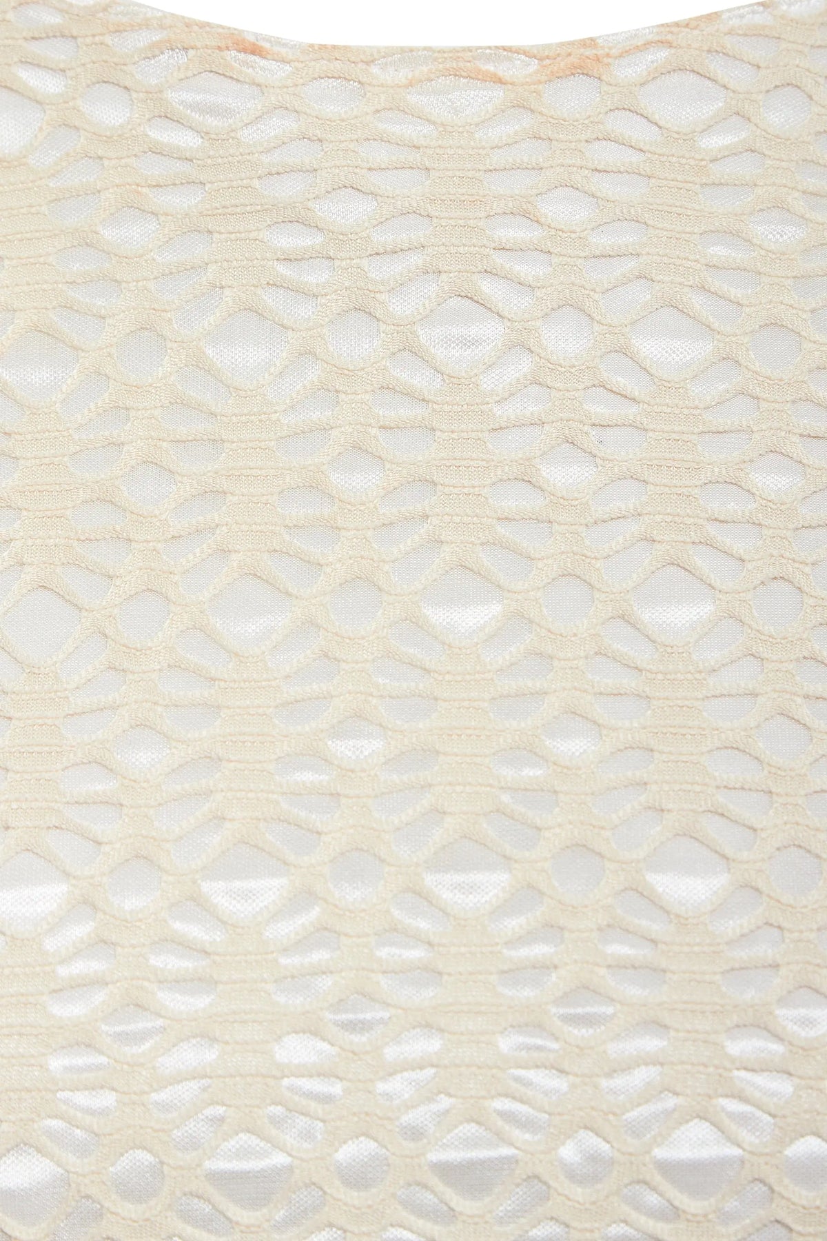 Close-up of Sarvin's Ivory Lace Backless Dress: cream-colored lace with a geometric hexagonal and oval pattern overlays a white background, showcasing the dress's textured detail.