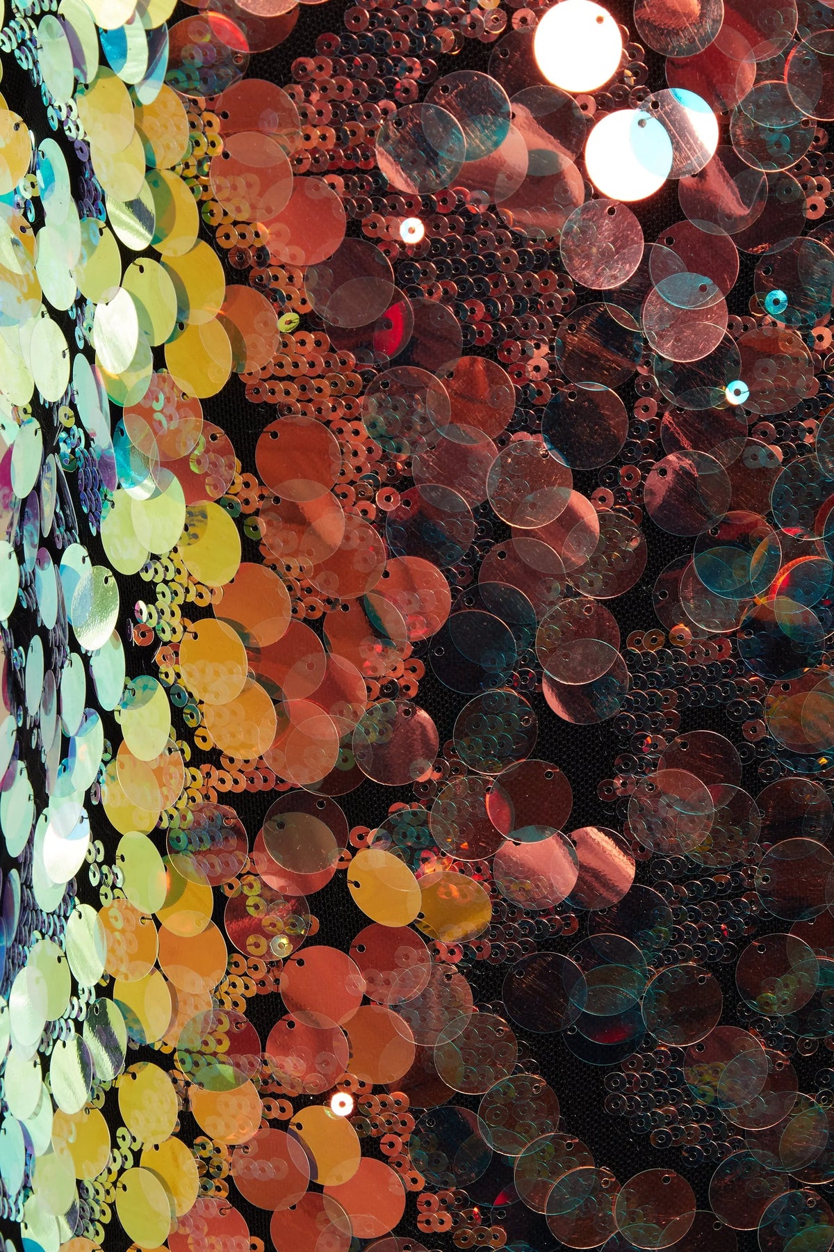 Close-up of overlapping yellow, gold, red, and iridescent sequins on dark fabric—details from the Sarvin High Neck Backless Sequin Mini Dress sparkling with color and texture as it catches the light.