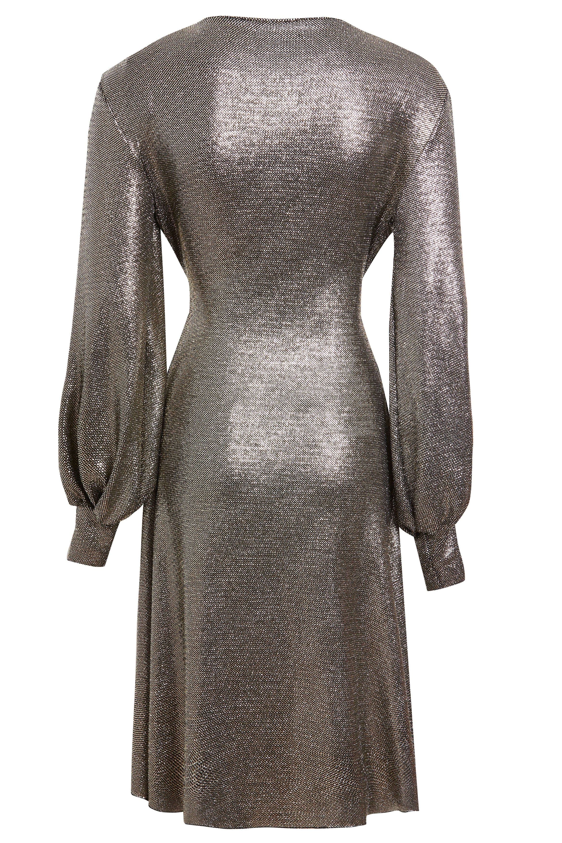 The Sarvin Long Sleeve Sequin Wrap Dress features a metallic silver finish, fitted waist, flared skirt, and loose cuffed sleeves. Its shiny, textured fabric makes it ideal for special occasions. Shown here from the back view.