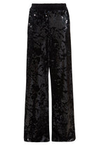 Sarvin Sequin Velvet Flared Trousers, handmade in the UK with an elastic waistband and shimmering black sequins, are showcased against a plain white background.