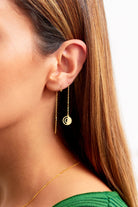 A close-up of a person with straight brown hair in a green top, wearing Sarvin's Circle Shape 18K Gold Drop Earrings—one featuring a thin bar and the other a round disc charm—for a minimalist look.