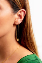 Close-up of a person with straight brown hair wearing Sarvin's Circle Shape 18K Gold Drop Earrings and a gold necklace, paired with a green ribbed top.