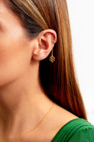 A close-up of a woman wearing Sarvin's Flower Shape 18K Gold Drop Earrings and a gold ear cuff. She has straight brown hair, a green top, and a thin gold necklace.