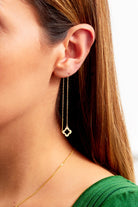 A close-up of a woman with straight brown hair and a green top wearing Sarvin's Clover Shape 18K Gold Threader Earrings, featuring a clover charm and paired with a thin gold necklace.