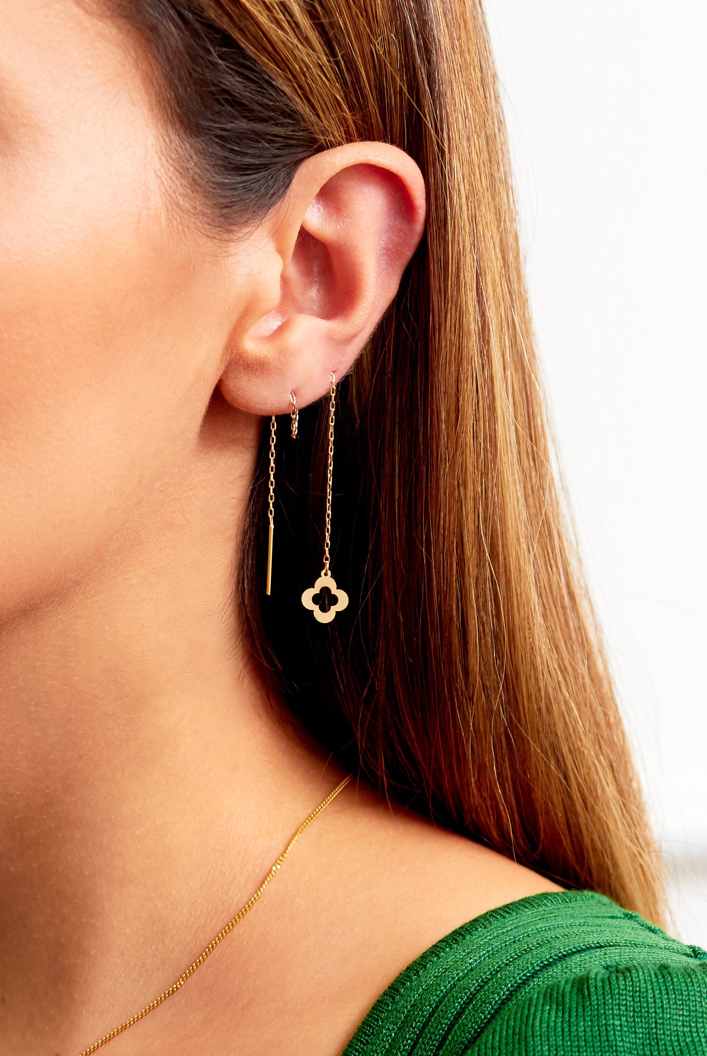 A woman with straight brown hair and a green top wears Sarvin Clover Shape 18K Gold Threader Earrings, featuring a sleek pull-through design and a clover-shaped drop charm.