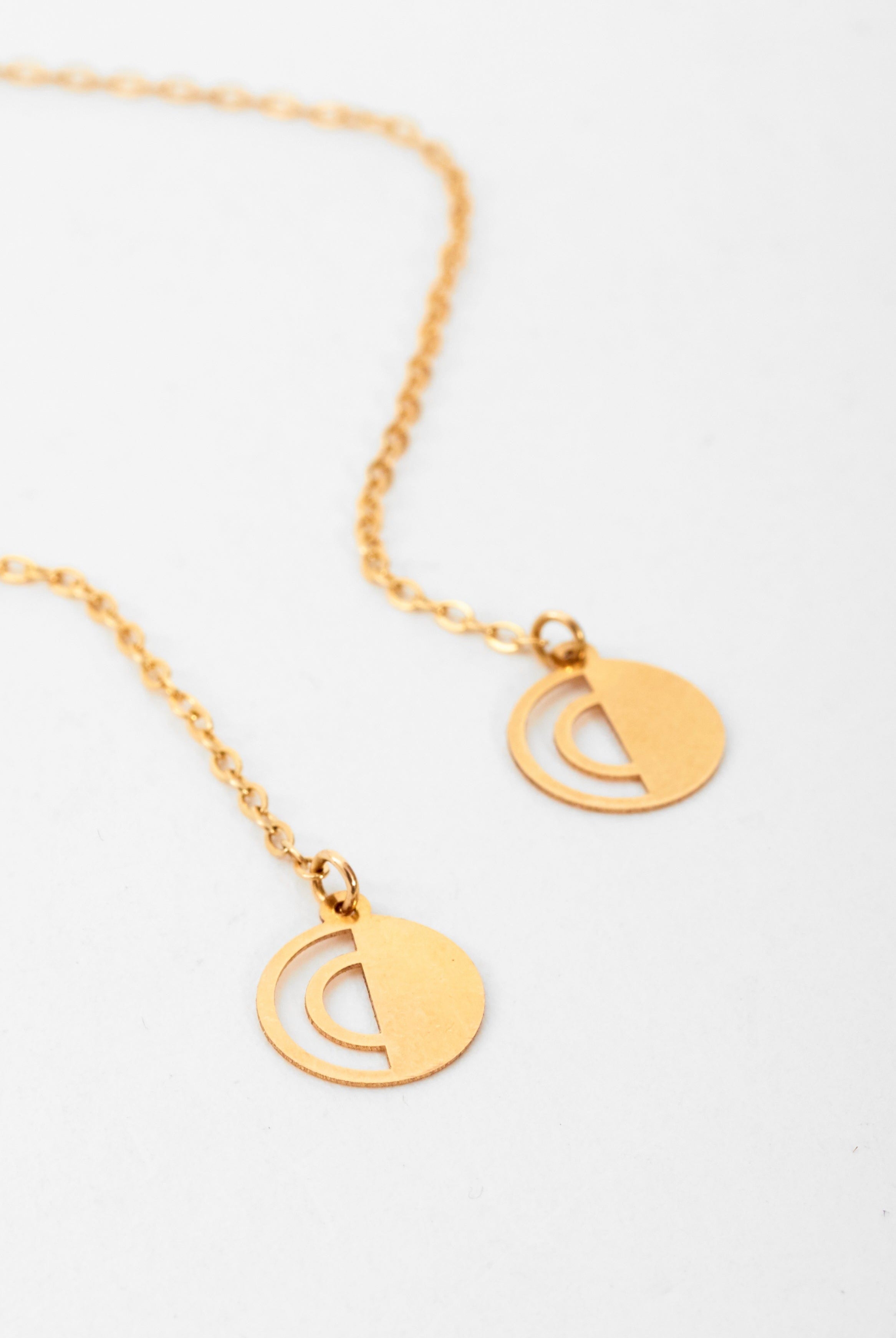 A close-up of Sarvin's Circle Shape 18K Gold Drop Earrings and a gold chain necklace with two round, cut-out semi-circle pendants, styled together on a plain white background for a minimalist look.