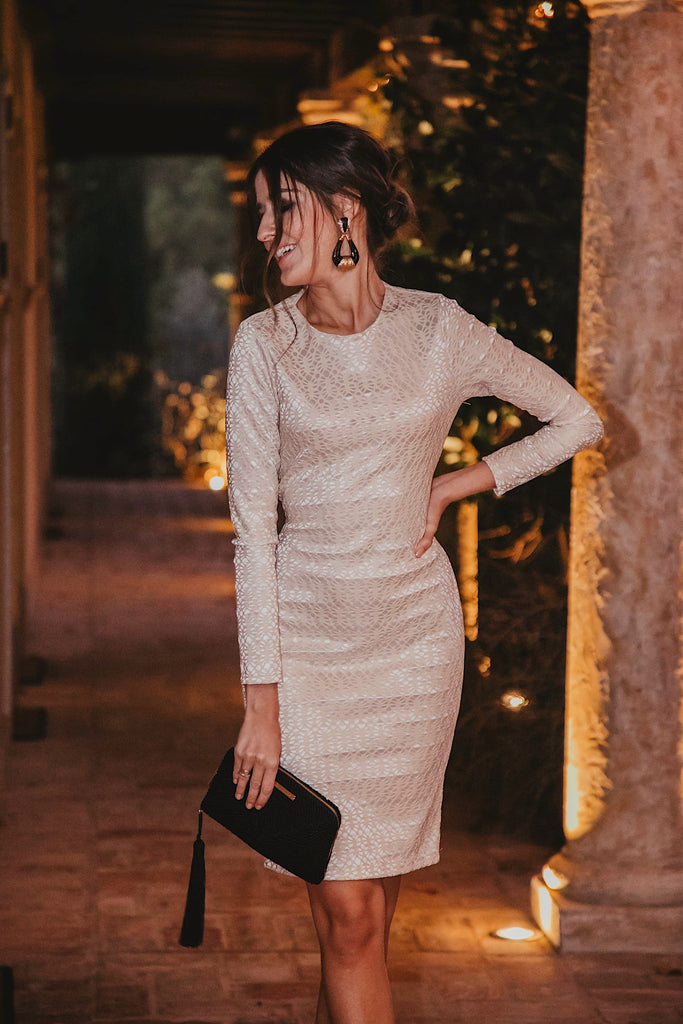 A woman wearing the Sarvin Ivory Long Sleeve Backless Dress and a black clutch.
