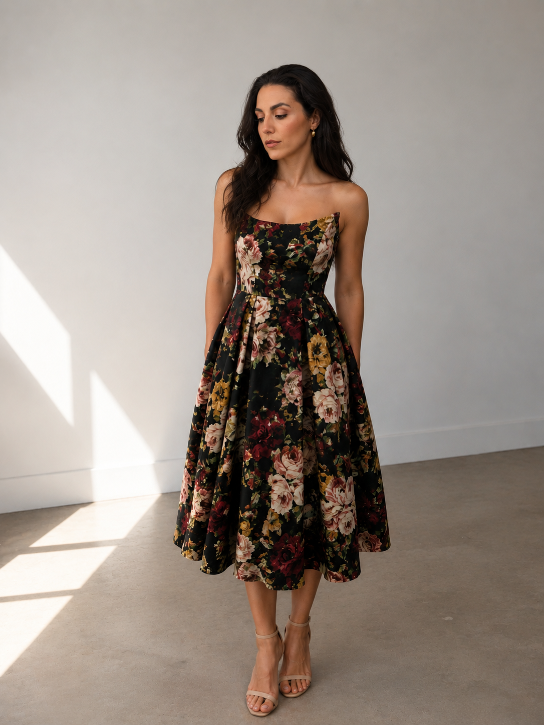 A woman stands indoors wearing the Sarvin Golshifteh Floral Corset Midi Dress with her hands in the pockets, long dark hair down, and looking slightly downward.