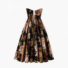 The Golshifteh Floral Corset Midi Dress by Sarvin features a strapless fitted bodice with lace-up back and dark floral pattern, finished with a flowing midi skirt for an elegant silhouette.