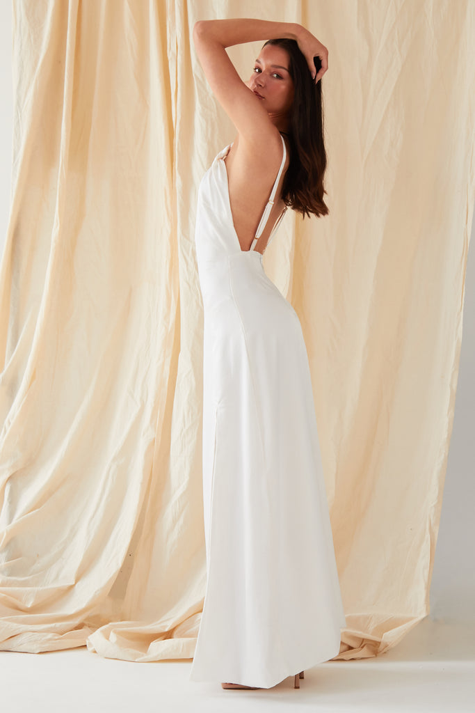 a woman in a Sarvin Asymmetric White Maxi Dress posing in front of a curtain.