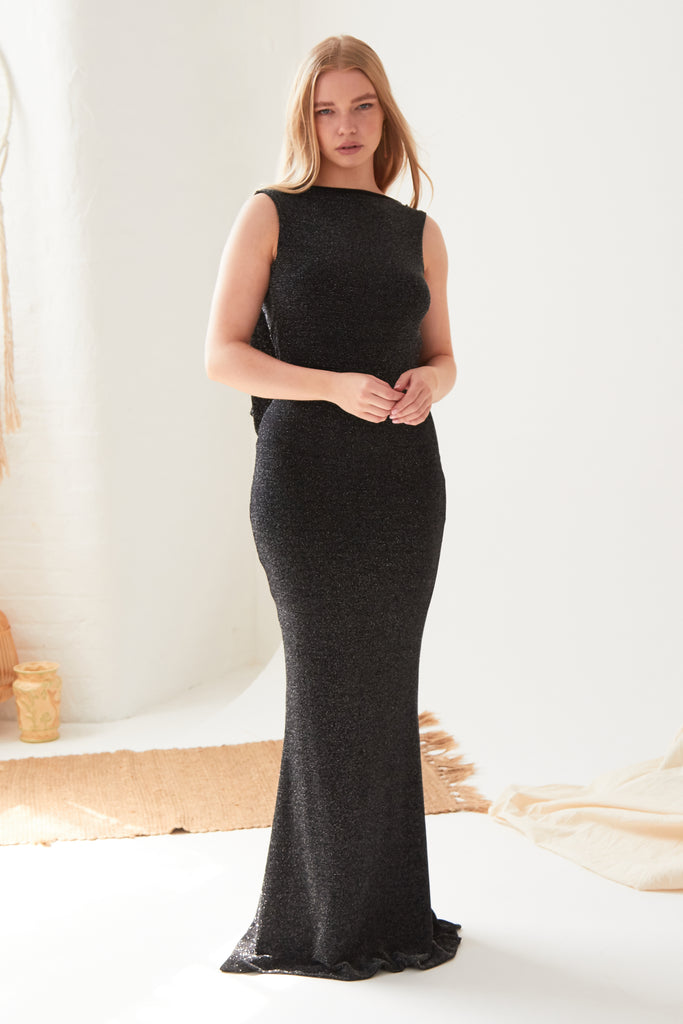 A woman is standing in a room wearing a Sarvin Black Cowl Back Gown.