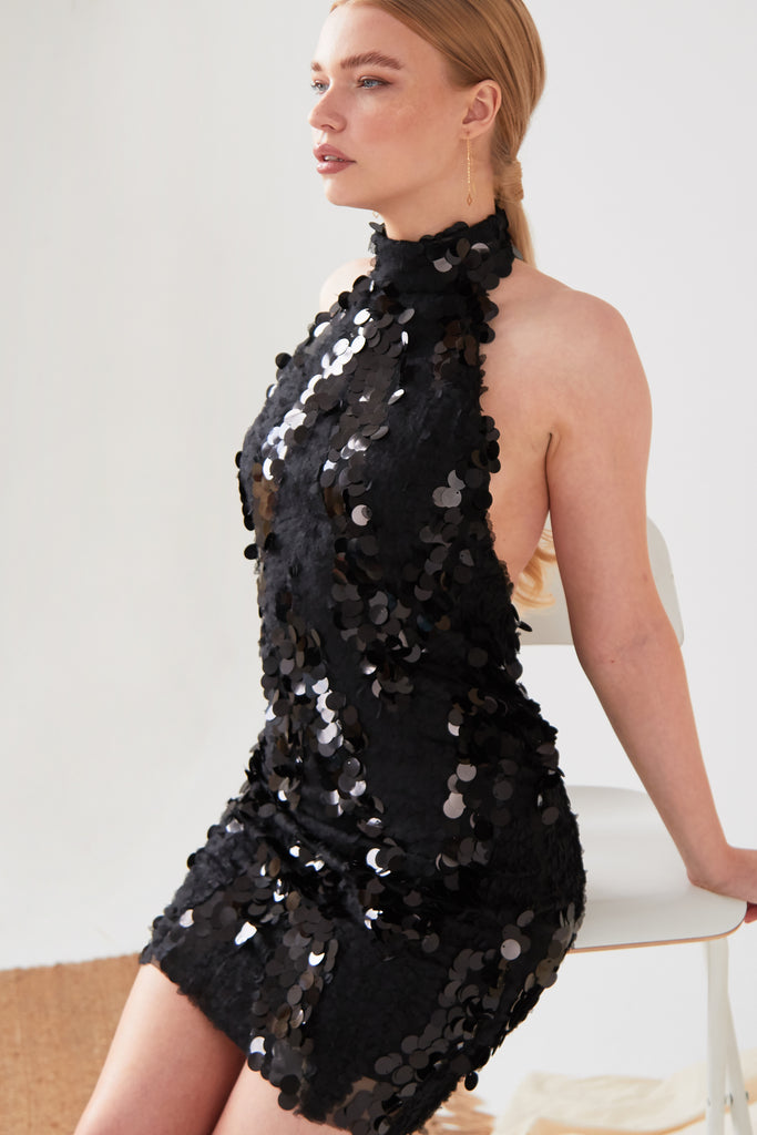 A woman wearing a Sarvin Black Backless Sparkly Dress posing on a chair.