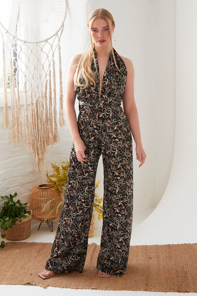 A woman is standing in a room wearing a Sarvin Floral Velvet Backless Jumpsuit.