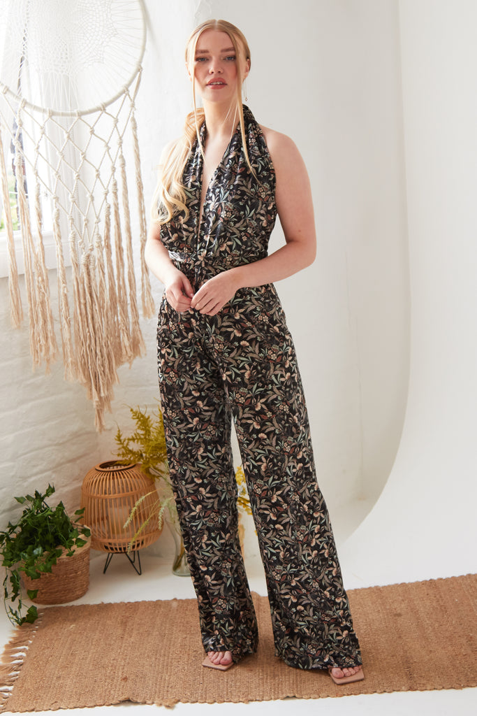 A woman in a Floral Velvet Backless Jumpsuit by Sarvin, standing in a white room.