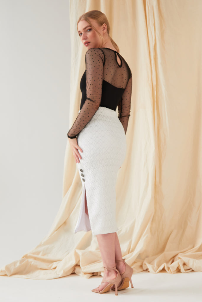 The model is wearing a Sarvin White Lace Bodycon Skirt with a sheer top.