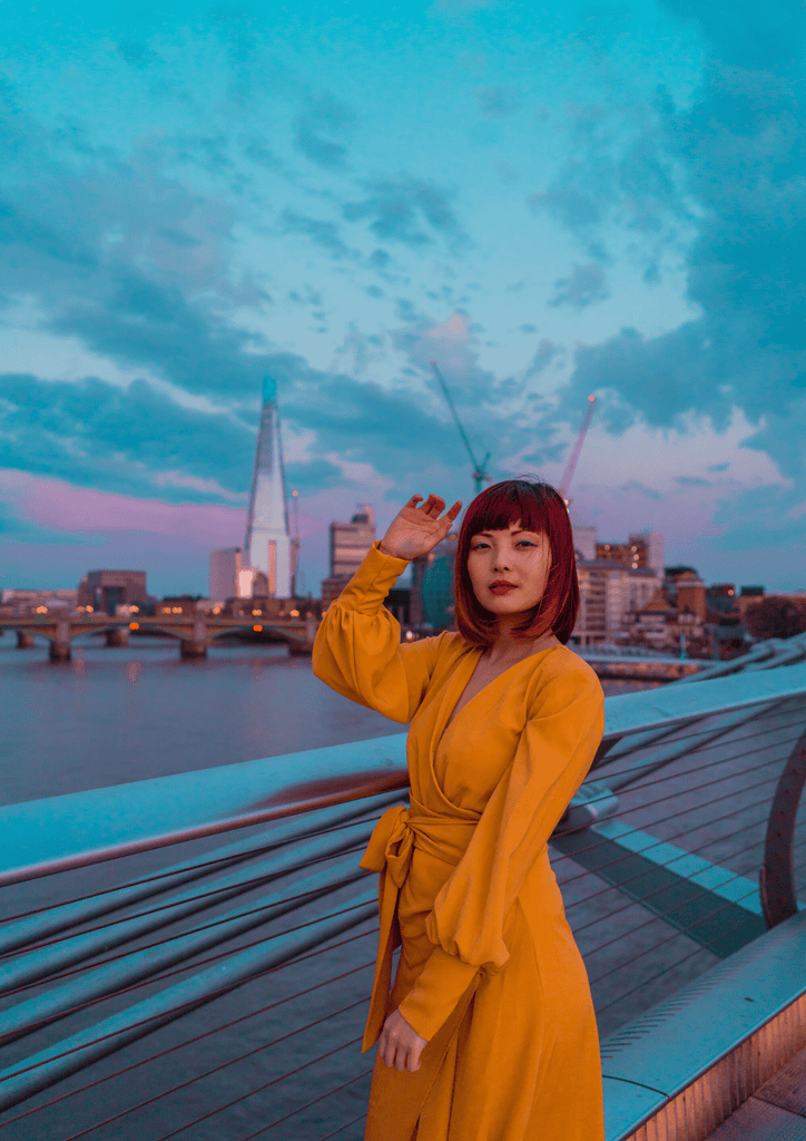 A woman in a Sarvin Mustard Wrap Dress standing on a bridge in London.